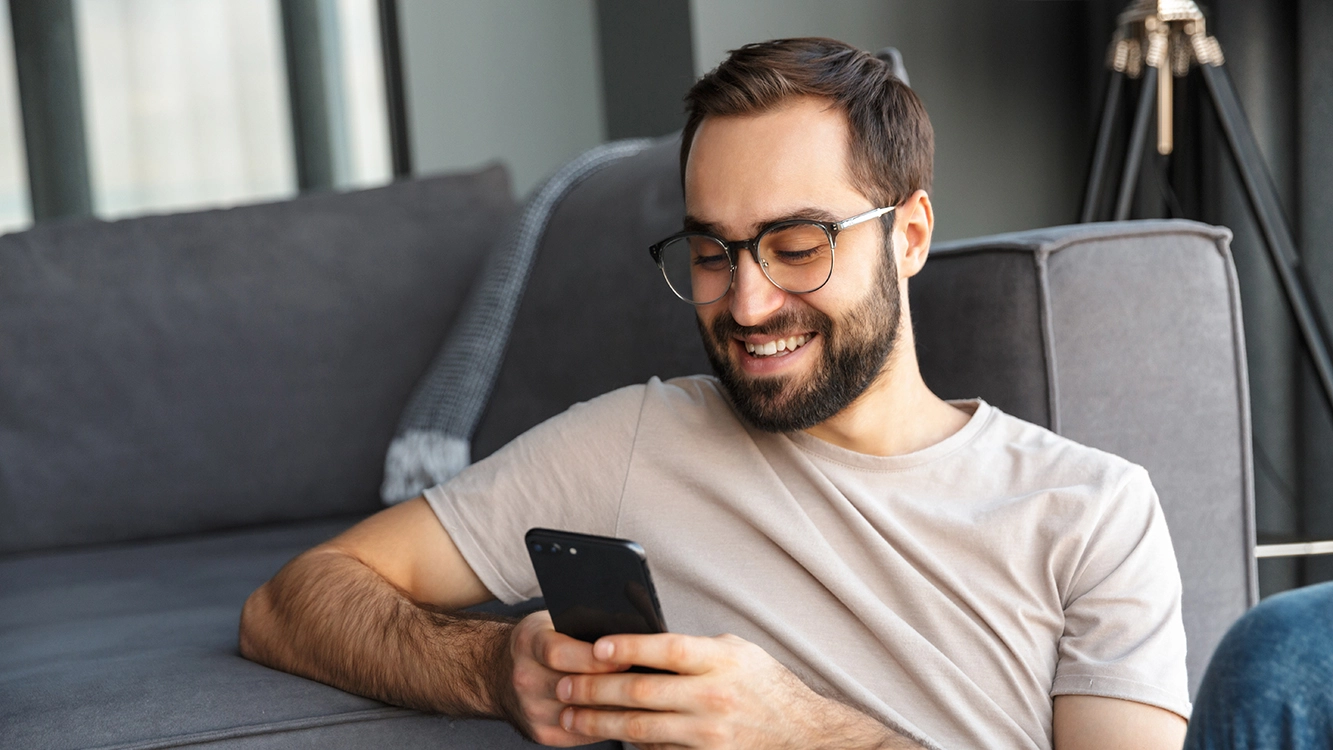 Homem sorrindo ao olhar para a tela do celular.