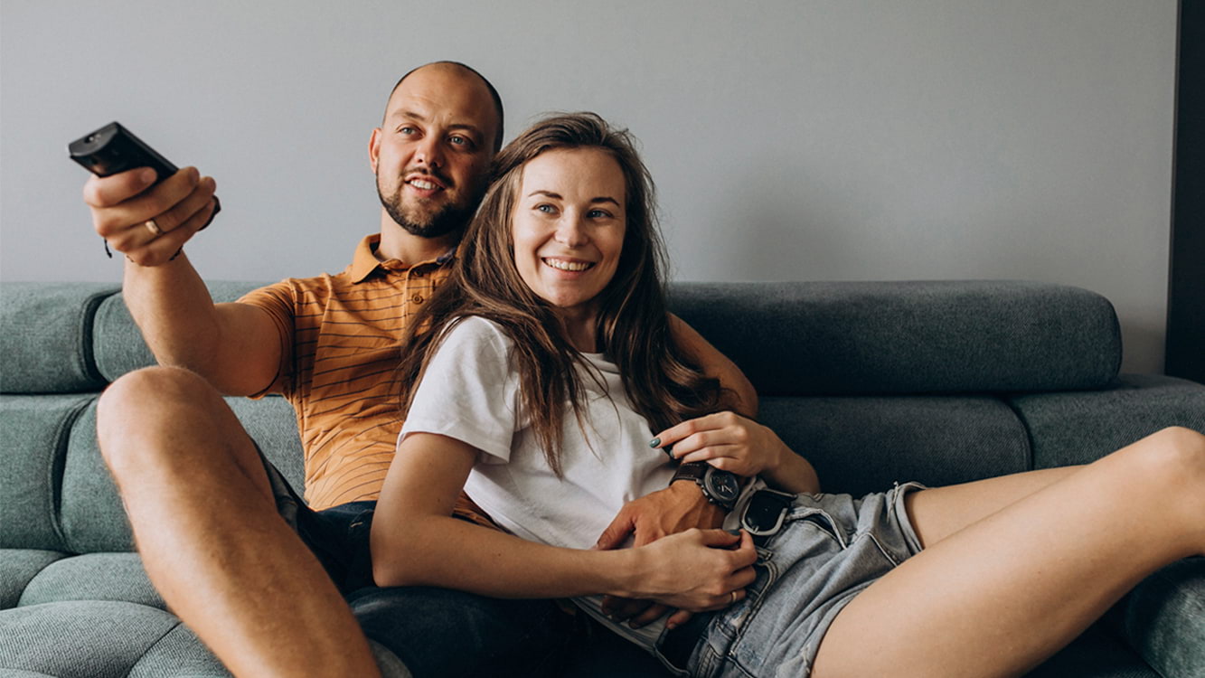 Casal sentado no sofá assistindo TV.