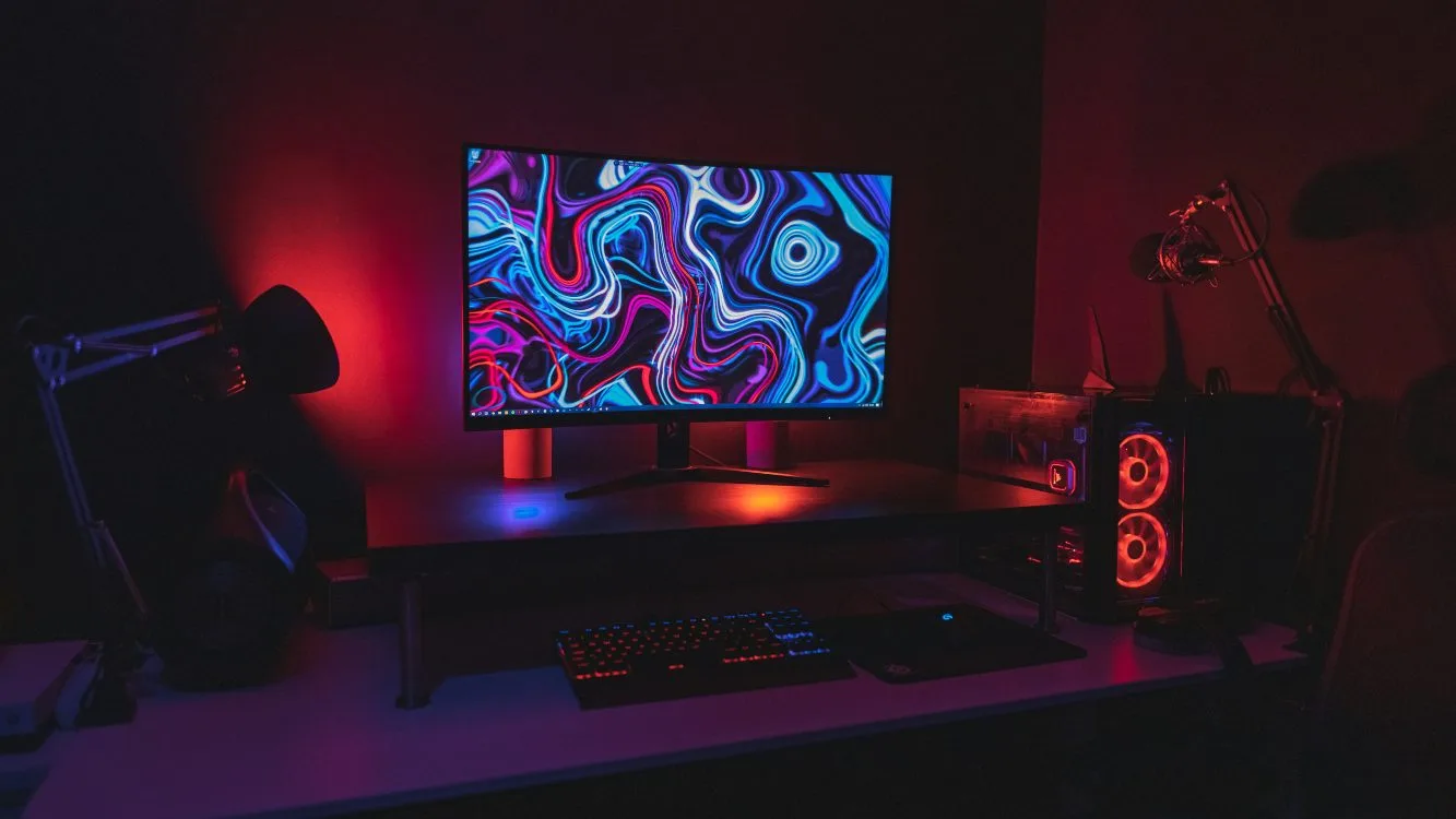 Computador gamer em cima de uma mesa. A tela exibe uma imagem colorida e abstrata. O quarto está escuro