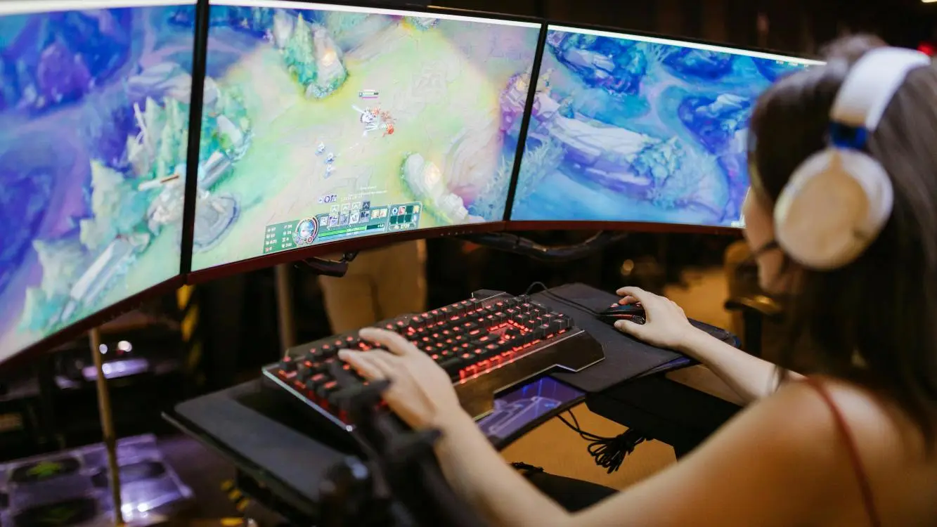 De costas, mulher de headset joga em frente a três monitores