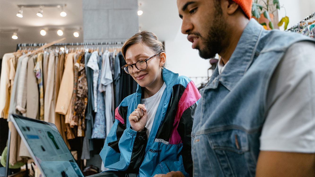 Dois jovens dentro de uma loja de roupas olhando a tela do computador.