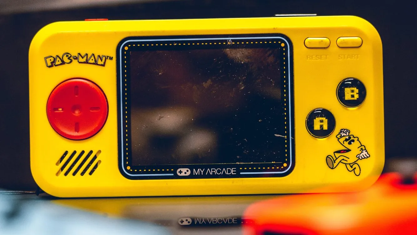 Videogame amarelo portátil, de formato horizontal, com a figura do Pac-Man