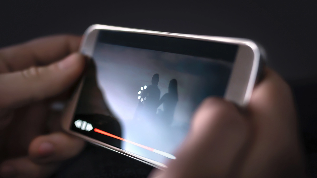 Mão segurando um smartphone que apresenta lentidão ao transmitir um vídeo.