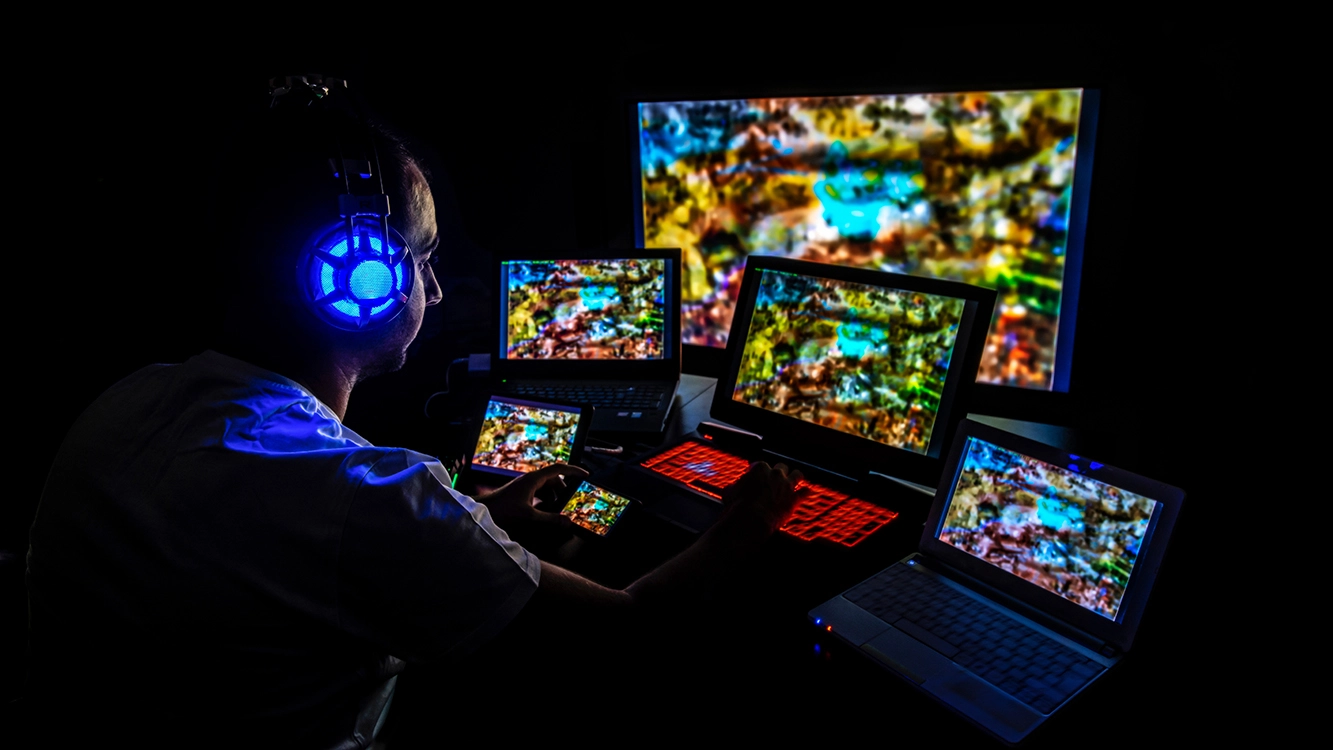 Homem com diversos computadores em sua mesa.