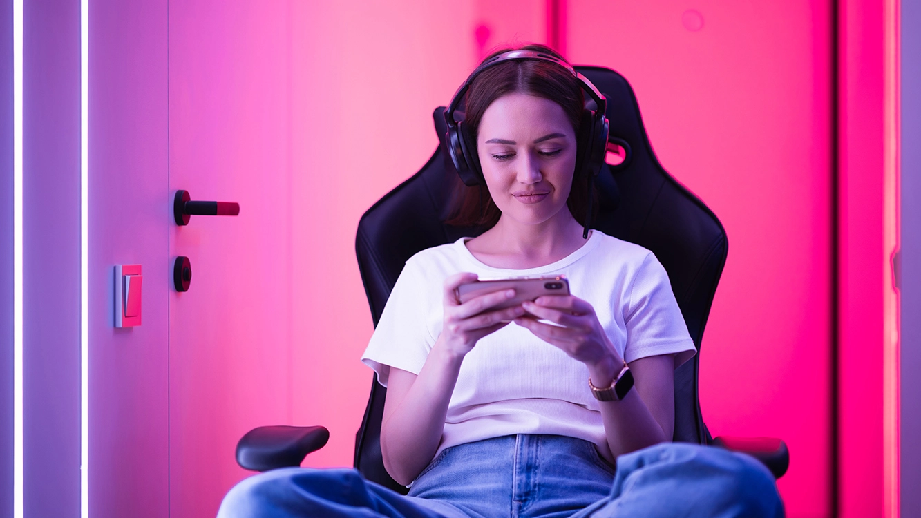 Menina sentada em uma cadeira gamer, jogando pelo celular.