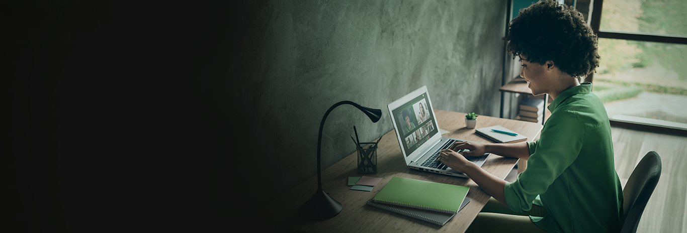 Moça de pele negra e camisa verde sentada sorrindo enquanto acessa um tablet