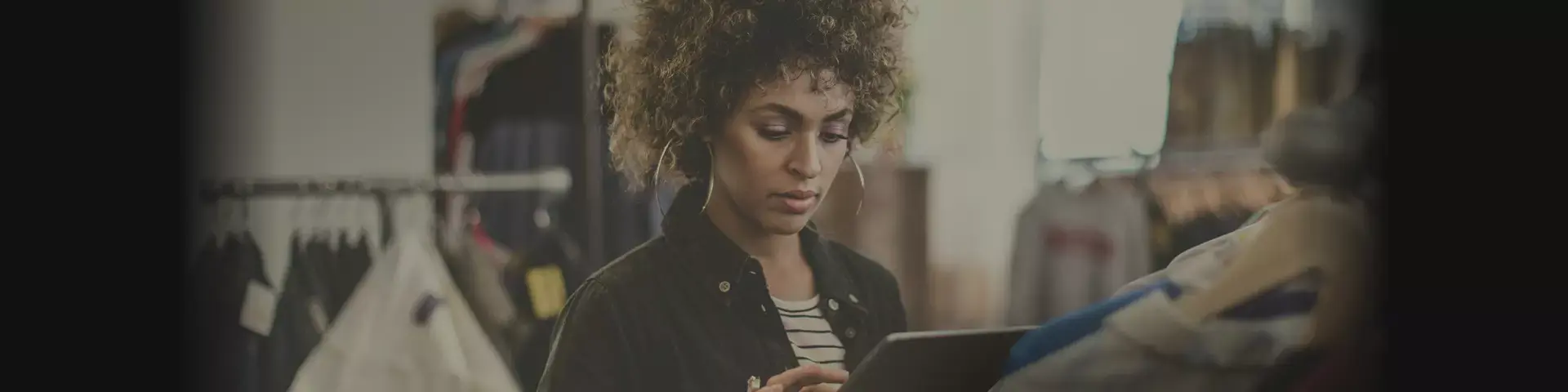 Na foto, uma mulher está dentro de uma loja enquanto parece consultar alguma informação em um tablet.