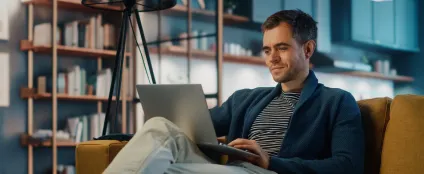 Homem, sentado no sofá de casa, usa laptop e internet Oi Fibra pra trabalhar