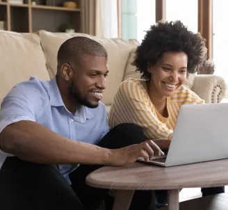 Homem e mulher, sentados na sala de casa, trocam o seu plano de internet Oi Fibra usando um computador