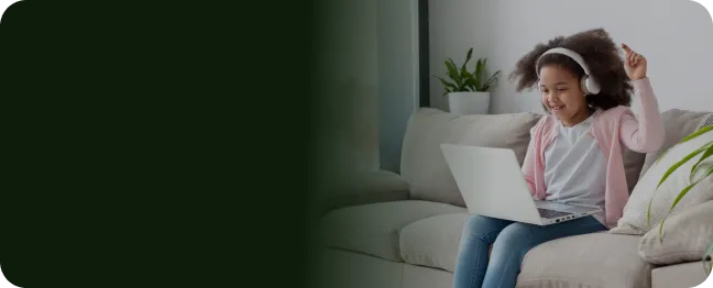 Menina, com fone de ouvido e sentada no sofá de casa, se diverte vendo desenhos online
