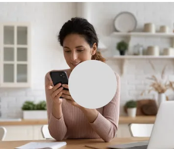 Na mesa da cozinha, mulher trabalha em um laptop conectado à internet fibra ótica enquanto usa o celular