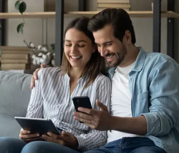 Mulher, segurando um tablet, e homem, segurando um celular, se divertem vendo um filme online