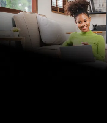 Mulher, sentada na sala de casa, usa laptop conectado à internet Oi Fibra