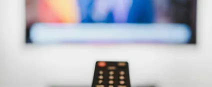 Controle remoto apontado pra Smart TV. Na tela, conteúdos de streamings
