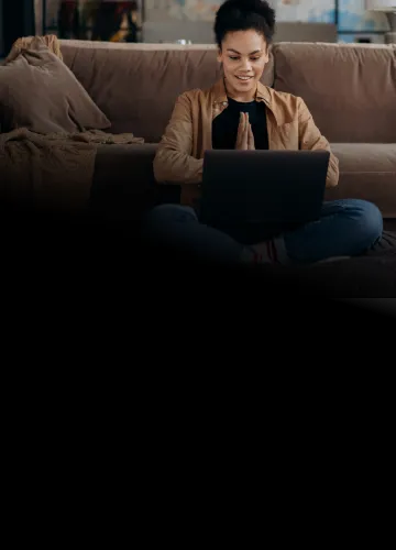 Sentada no chão da sala de casa, mulher usa computador conectada à internet Oi Fibra
