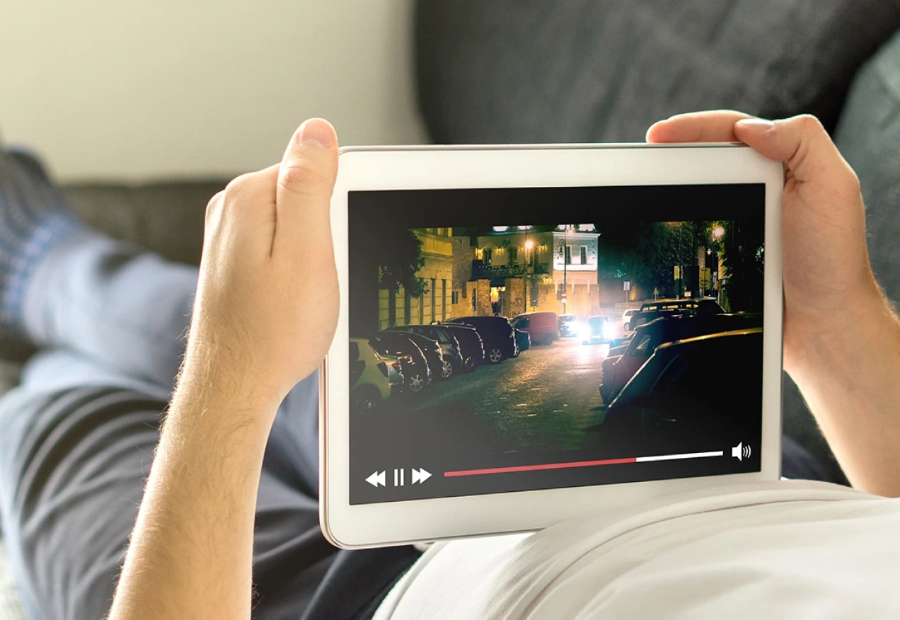 Pessoa segurando um tablet e assistindo a um vídeo de carros numa rua à noite e usando a melhor plano de internet residencial.