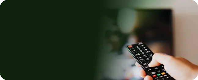 Uma mão segura um controle remoto em frente a uma TV pra assistir conteúdos do seu streaming usando Oi Fibra.