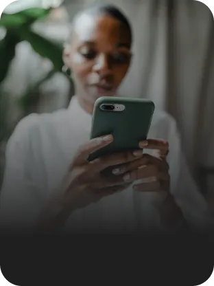 Mulher utilizando celular conectado com a internet fibra da Oi, com plantas ao fundo, transmitindo um ar de conforto e estilo.