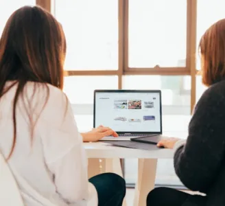 De costas e de casaco, duas mulheres usam um computador pra navegar na internet