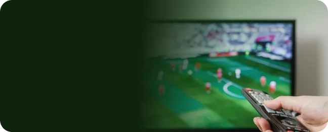 Imagem mostra uma mão segurando um controle remoto enquanto a pessoa assiste a uma partida de futebol na TV por streaming com a internet 1 Giga da Oi.