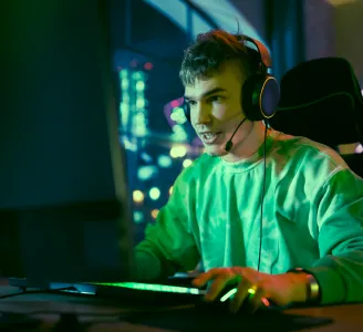 Jovem gamer concentrado jogando online  com Oi Fibra 1 Giga em computador com headset, em um quarto gamer iluminado por luzes coloridas.