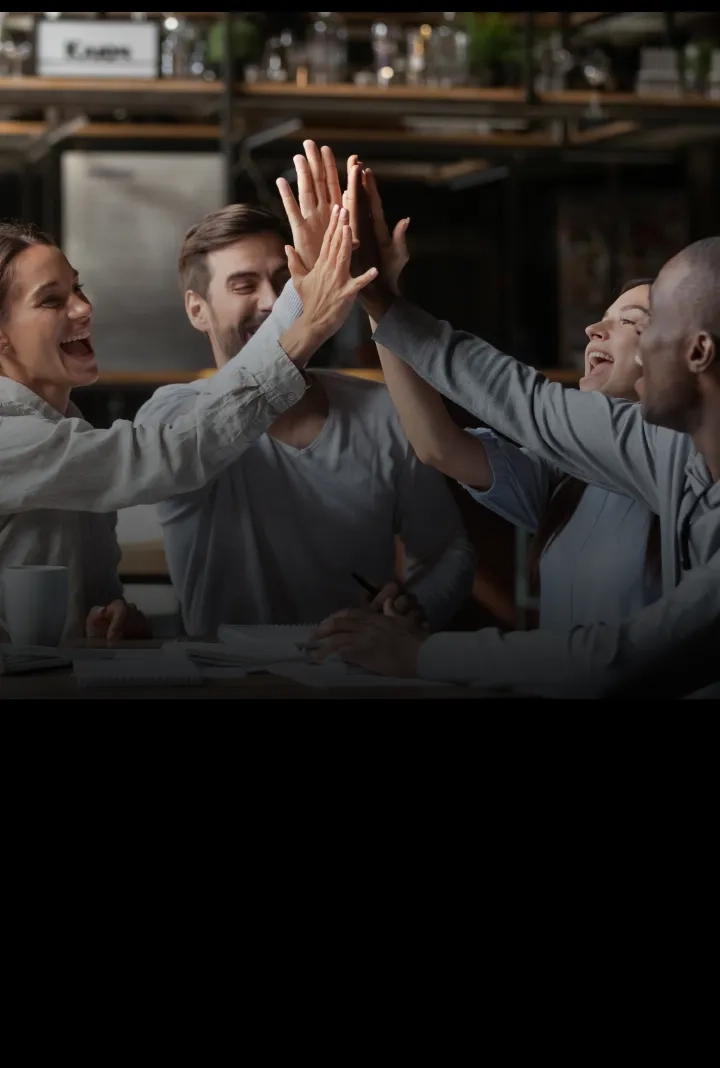 Foto de quatro pessoas num escritório de trabalho fazendo high five e comemorando