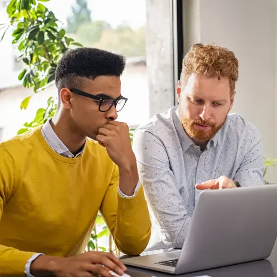 Dois homens estão focados trabalhando em um laptop.