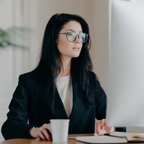 Mulher concentrada com oculos no computador.