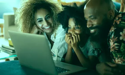 Imagem mostra três pessoas reunidas com fisionomia feliz em frente a tela de um notebook