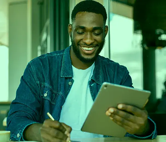 Homem sorrindo utilizando um tablet enquanto na outra mão segura uma caneta