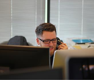 Homem em um escritório atendendo o telefone enquanto trabalha no computador