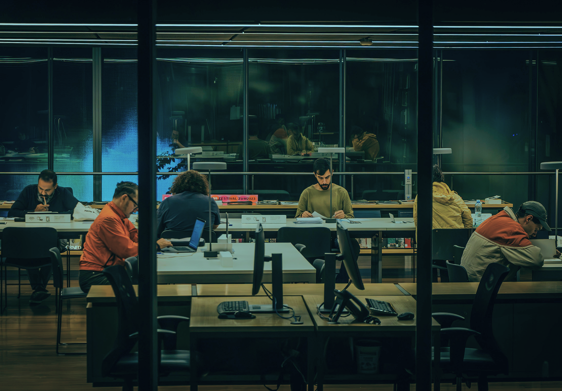 Pessoas trabalhando e estudando em ambiente moderno de escritório e coworking durante a noite, representando a sala de imprensa.